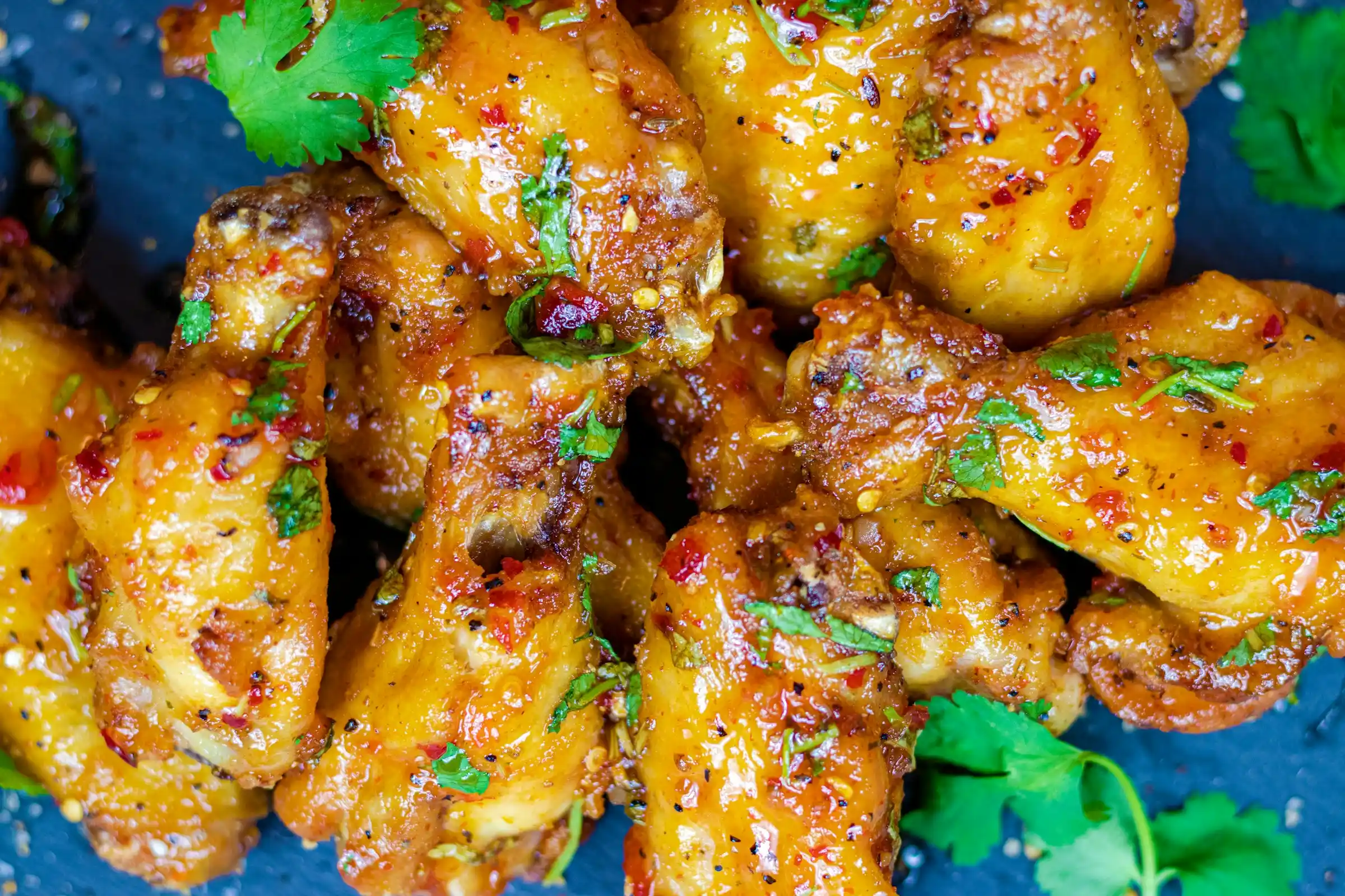 Crispy golden air fryer chicken wings piled on parchment paper with dipping sauces and celery sticks on a rustic wooden table