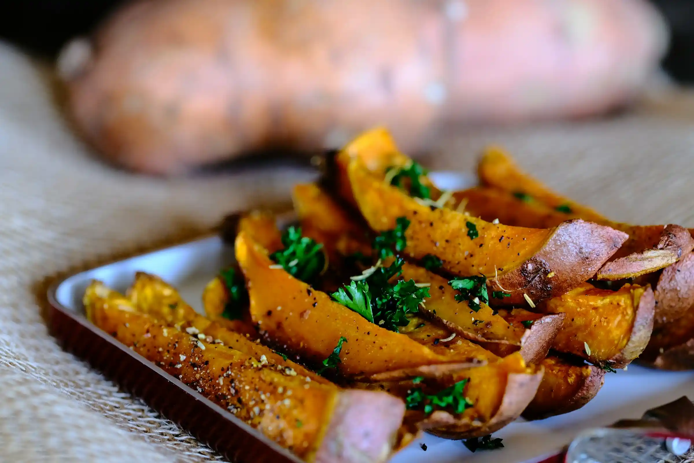 Crispy air fryer sweet potato fries with a whole baked sweet potato split open on a white plate with dipping sauce