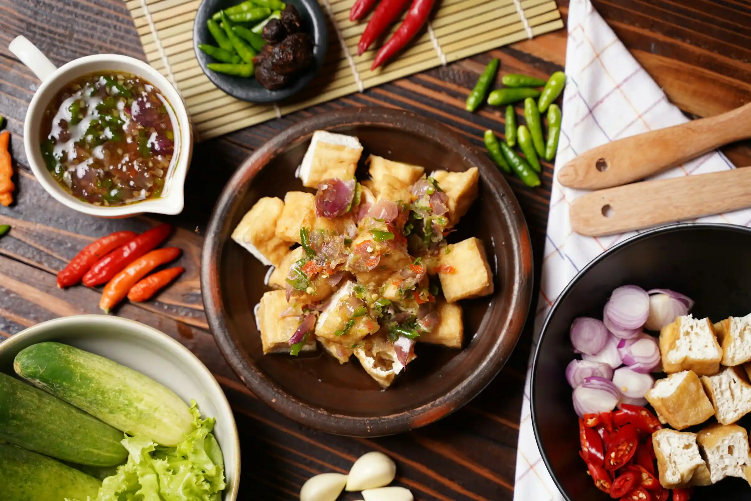 Crispy golden air fryer tofu cubes in a bowl with sesame seeds and sliced green onions on a rustic wooden table